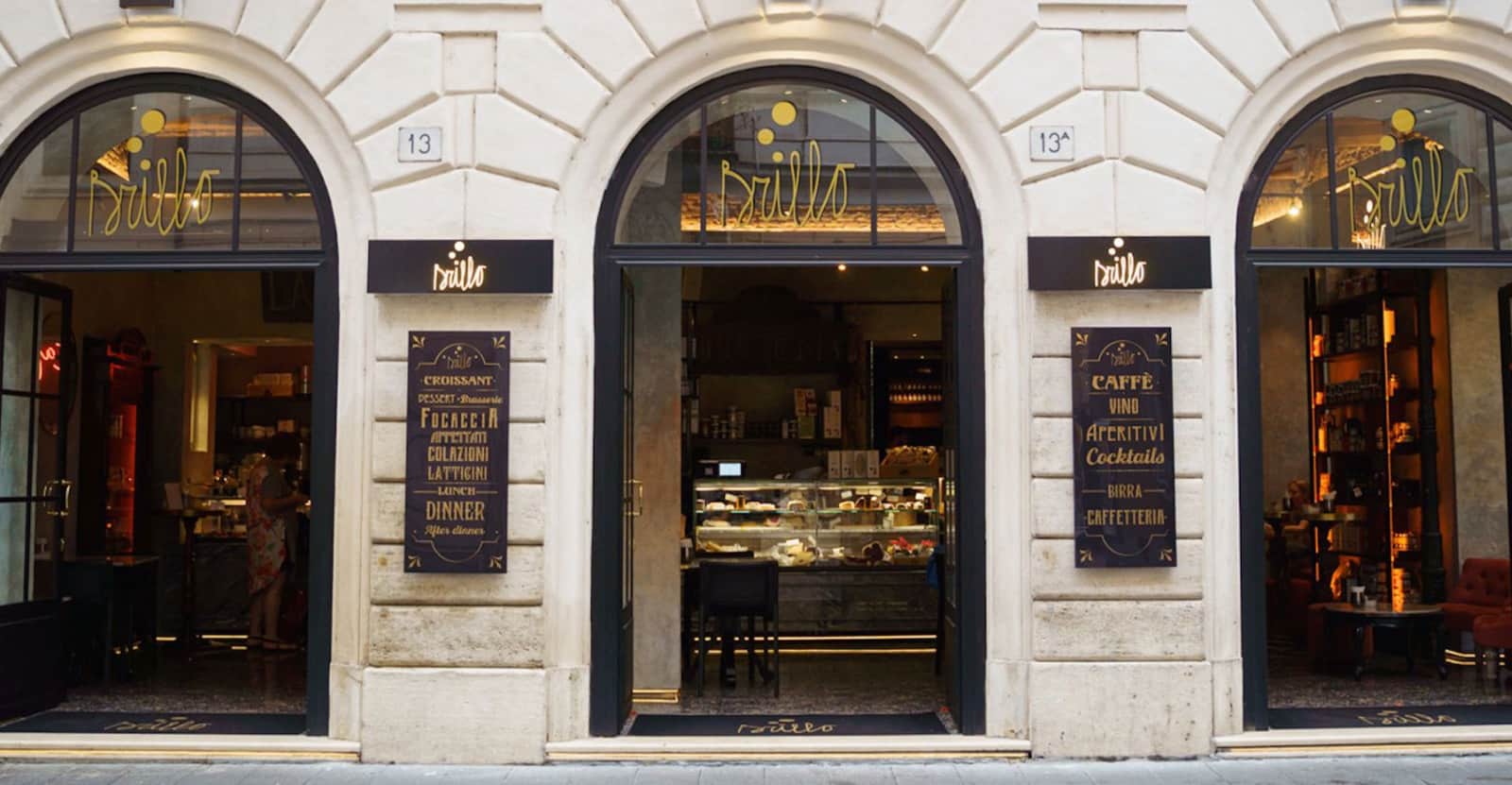 Facciata in pietra chiara con tre archi neri e insegne dorate con la scritta Brillo.