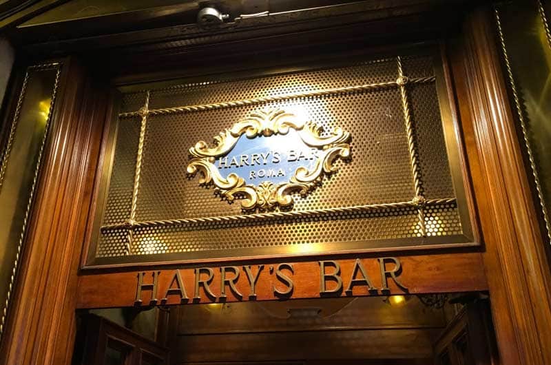 Insegna in ottone con targa ovale scritta "Harry's Bar Roma", sopra la scritta in rilievo "Harry's Bar" sull'architrave in legno.