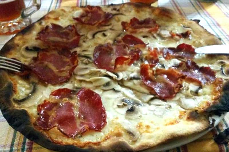 Pizza rotonda con fette di prosciutto crudo, funghi champignon a fette e formaggio fuso.