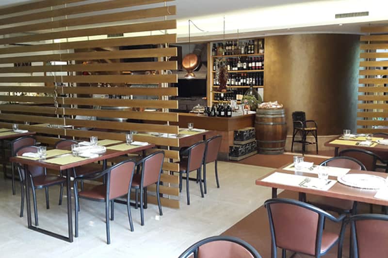 Sala ristorante con divisori in listelli di legno, tavoli apparecchiati e banco con bottiglie di vino a muro.