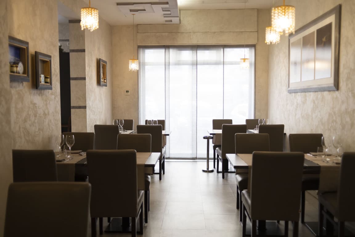 Sala da pranzo con tavoli apparecchiati e sedie in pelle scura, illuminata da lampadari a goccia dorati.