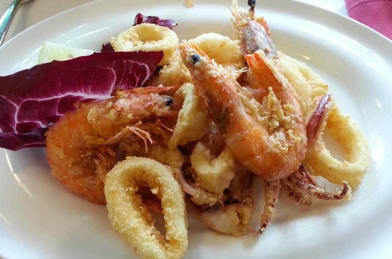 Piatto di gamberi e anelli di calamari fritti impanati, servito con radicchio rosso su piatto bianco.