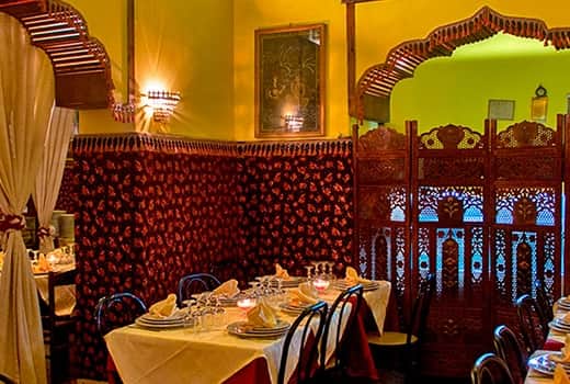 Sala da ristorante con pareti a motivi rossi e dorati, tavoli apparecchiati e un separè in legno intagliato.