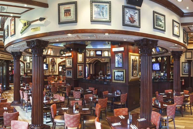 Sala di ristorante con colonne in legno scuro, pareti chiare coperte di quadri incorniciati e una chitarra elettrica esposta.