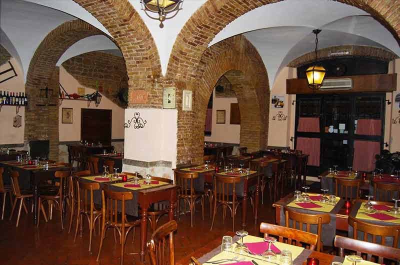 Sala con volte in mattoni, archi in muratura e tavoli apparecchiati con tovaglie gialle e tovaglioli rossi.