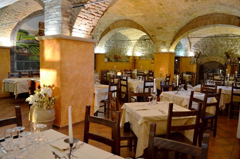 Sala da pranzo con soffitti a volta in mattoni, colonne color ocra e tavoli apparecchiati con candele.