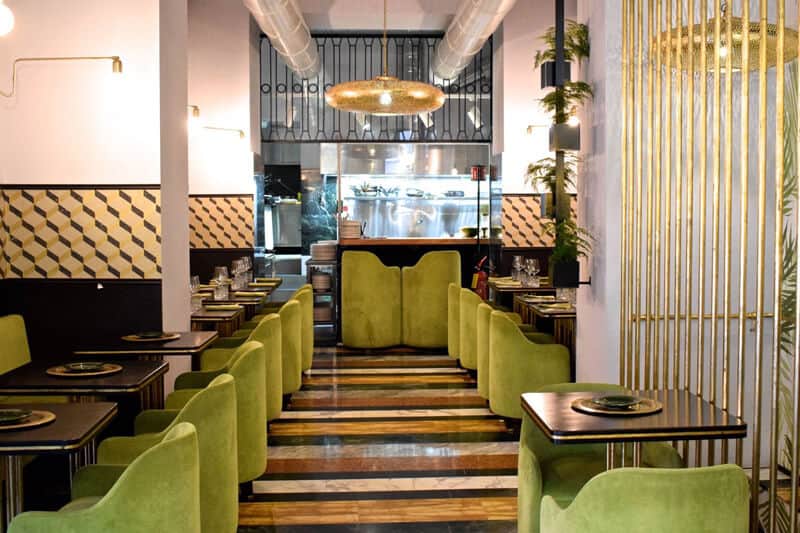 Sala da ristorante con poltroncine verdi ai lati di un corridoio in marmo a righe, lampade dorate a sospensione sul soffitto.