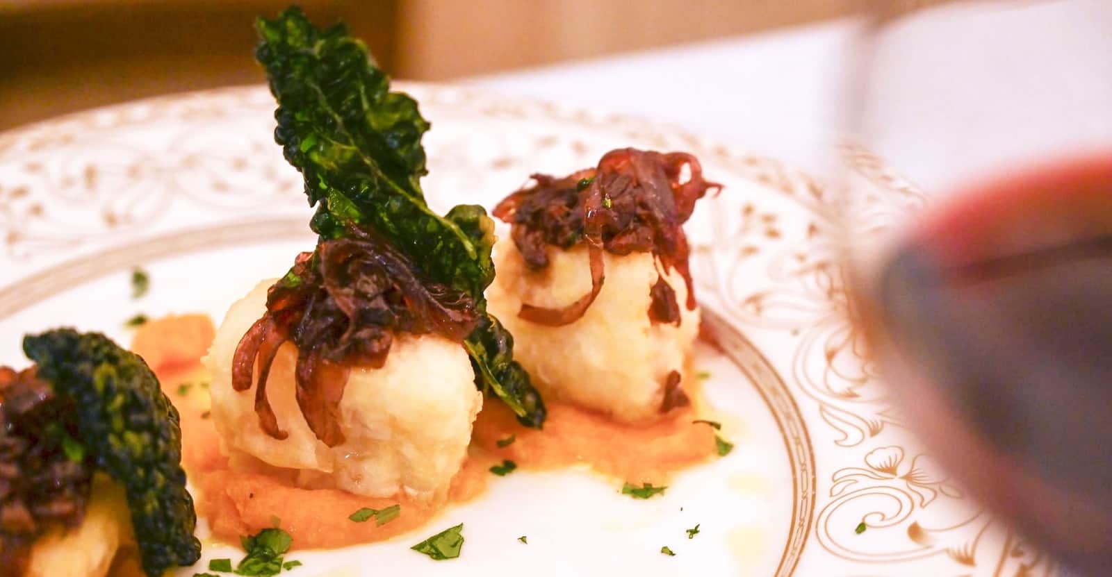 Involtini fritti dorati con cipolla croccola e foglia di cavolo nero, su crema arancione in un piatto decorato oro.