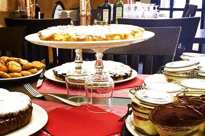 Torte e dolci su piatti impilati con calici di vetro, in tavola con altri dessert in vasetti di vetro.