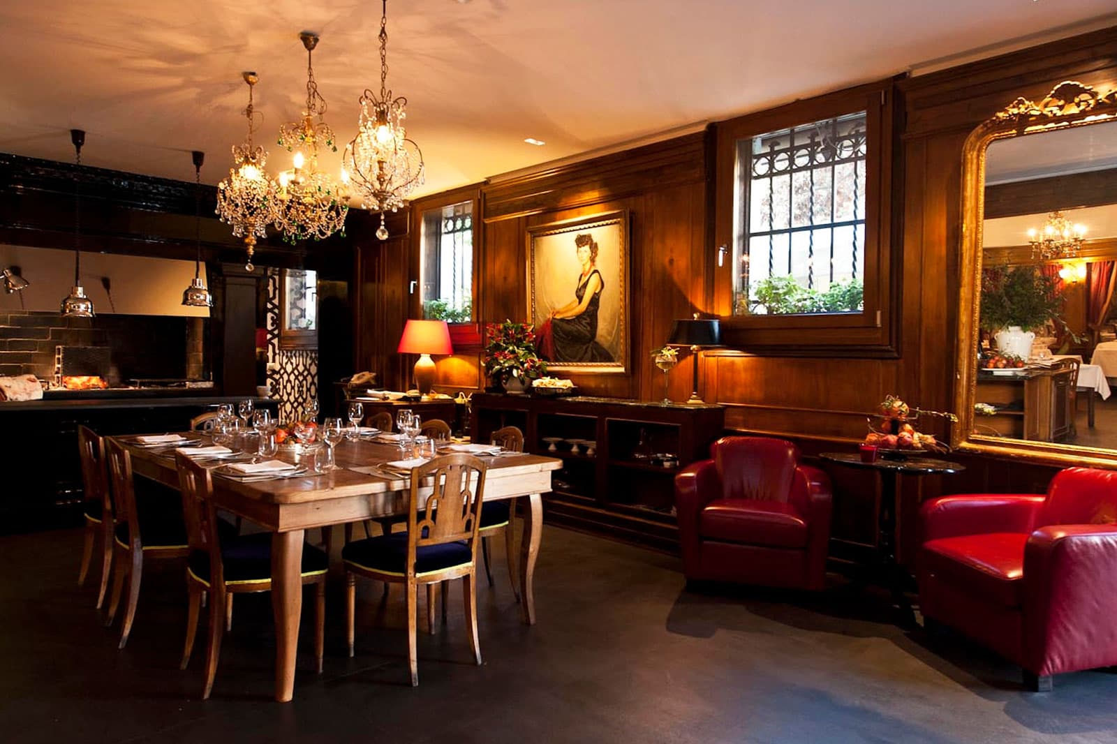 Sala da ristorante con boiserie in legno scuro, tavolo apparecchiato e due poltrone in pelle rossa.
