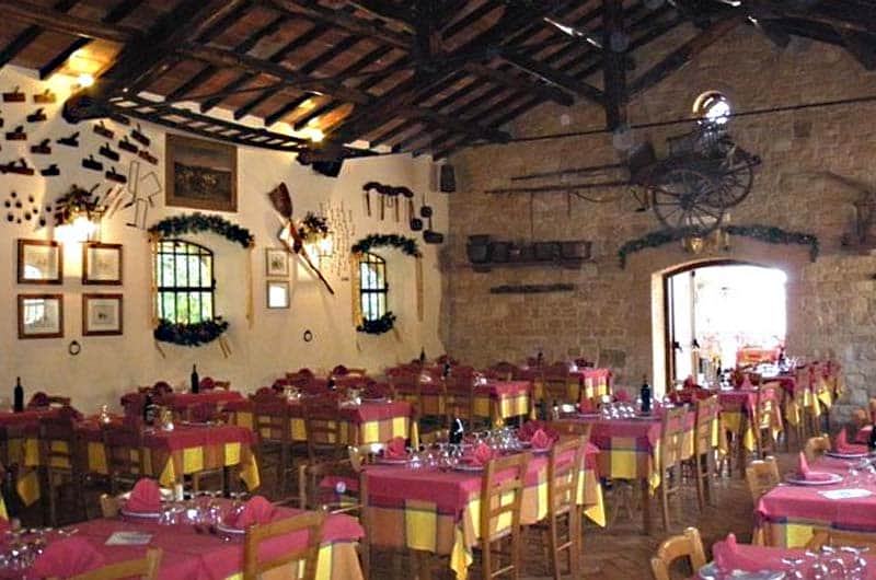 Sala da pranzo rustica con tetto in travi di legno, tavoli con tovaglie rosse e gialle e pareti in pietra.