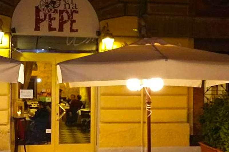 Facciata gialla di sera con insegna PEPE, lampioni accesi e ombrelloni bianchi in primo piano.