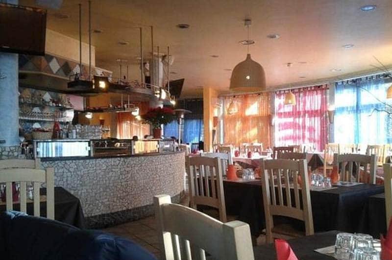 Sala da ristorante con bancone in mosaico chiaro e tavoli apparecchiati sotto lampade a sospensione.