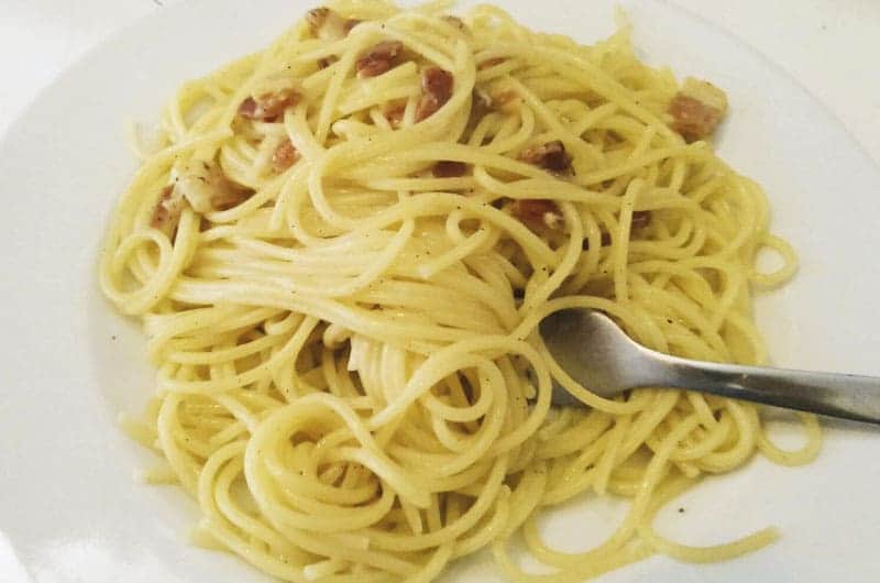 Spaghetti attorcigliati con pezzetti di carne rosolata e pepe nero, forchetta appoggiata sul bordo destro del piatto.