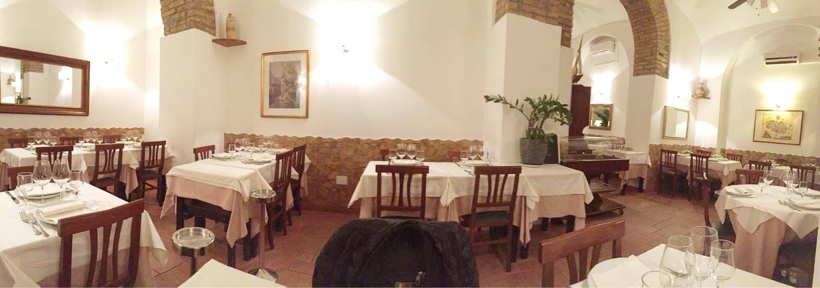 Sala da pranzo con soffitti a volta in mattoni, tavoli apparecchiati con tovaglie bianche e bicchieri da vino.