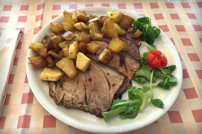 Piatto con fette di carne arrosto, patate a cubetti rosolate, insalata verde e un peperoncino rosso.